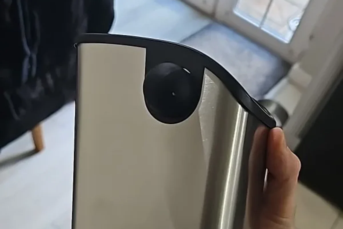 The brushed stainless steel body of the Barwright knock box, held in one hand